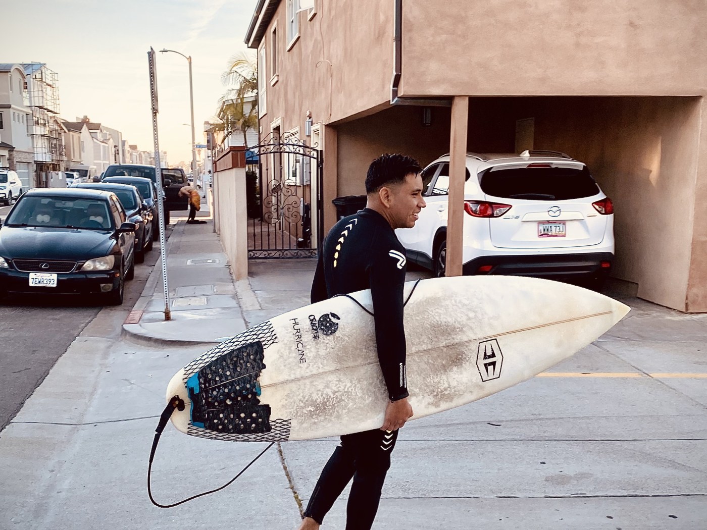 Fredy in a wetsuit carrying a surfboard